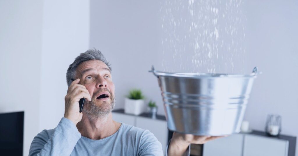 A concerned homeowner on the phone looking at water damage on their ceiling from a burst pipe